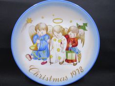 a blue and white plate with three little angels on it that says christmas 1908 in gold lettering