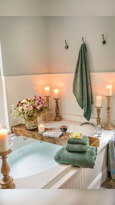 a bathtub with candles, towels and flowers in the corner next to it is filled with soap