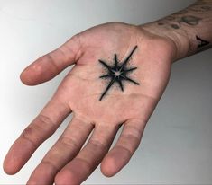 a person's hand with a small black star tattoo on the middle of it