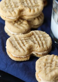 peanut butter sandwich cookies sitting on top of a blue towel next to a glass of milk