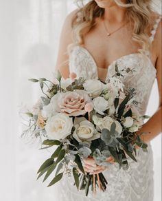 a bride holding a bouquet of white and pink flowers with greenery in her hands