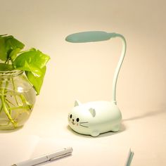 a white cat lamp sitting next to a glass vase filled with water and green plants