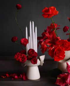 two white vases filled with red flowers and candles