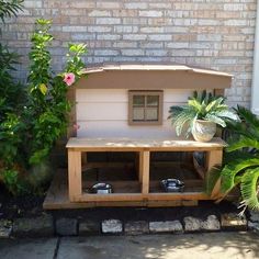 a dog house made out of pallets in front of a brick wall with potted plants