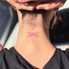 a woman's neck with a small pink dragonfly tattoo on her left side