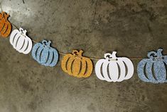 a string of paper pumpkins hanging from a line on a concrete wall with glitter paint