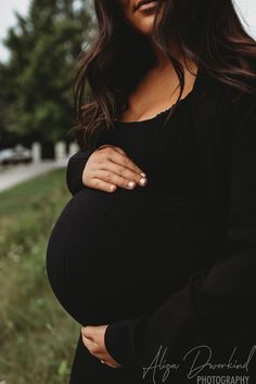 a pregnant woman poses for a photo in the grass with her hands on her belly