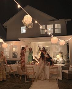 a group of women standing in front of a house with lights strung from the roof