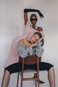 two women sitting on top of a chair with one holding the other's head