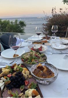 a long table with plates and bowls of food on it next to the ocean at sunset