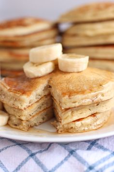 pancakes with bananas and syrup on a white plate next to a stack of pancakes that have been cut in half