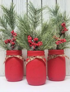 three red mason jars with pine branches and berries tied around them