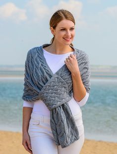 a woman standing on the beach wearing a gray knitted shawl over her shoulders