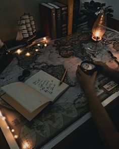 a person sitting at a desk writing on a map with candles around it and books