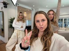 three women standing in a living room with one holding up the peace sign and the other pointing at the camera