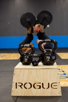 a man is lifting two black kettles on top of a wooden stand in a gym