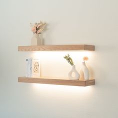 two white vases are sitting on a shelf with some books and flowers in it