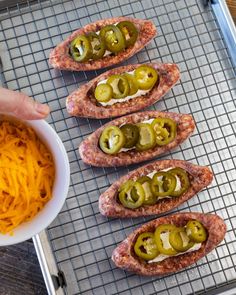 several hot dogs with jalapenos and cheese are on a cooling rack next to a bowl of macaroni and cheese