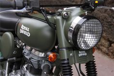 a green motorcycle parked next to a stone wall with the words royal enfield on it