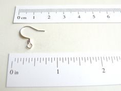 a pair of silver earrings sitting on top of a measuring ruler next to each other