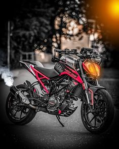 a red and black motorcycle parked on the side of a road at night with its lights on