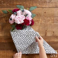 someone is wrapping flowers in a polka dot paper bag on a wooden table with wood planks