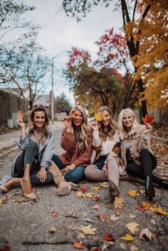 three women sitting on the ground in front of trees with leaves all around them and one woman taking a selfie