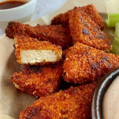 some fried food is on a plate with dipping sauces and celery sticks