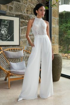 a woman standing in front of a stone wall wearing white pants and a halter top