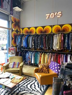 a store with lots of colorful clothing hanging on the wall and chairs in front of it