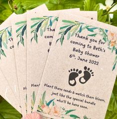 four baby shower tags with pink flowers and green leaves in front of some plants on the ground