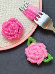 two crocheted flowers and a fork sitting on a table next to each other