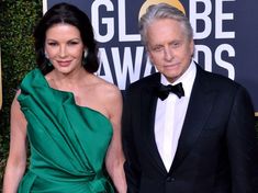 an older man and woman standing next to each other on a red carpet wearing green dresses