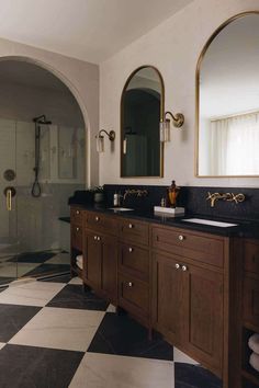 a bathroom with black and white checkered flooring, gold framed mirrors and two sinks