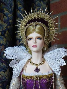 a close up of a doll wearing a purple and gold dress with white laces