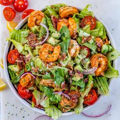 a salad with shrimp, lettuce, tomatoes and onions in a white bowl