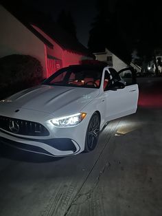 a white sports car parked in front of a house at night with its lights on