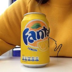 a woman sitting at a table with a can of fanta lemon soda in front of her