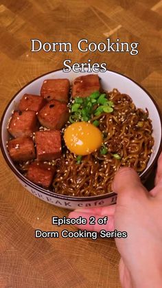 a bowl filled with noodles and meat on top of a wooden table next to a person's hand