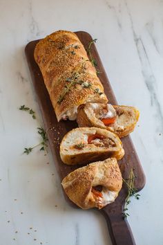 a wooden cutting board topped with bread covered in meat and cheese