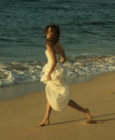 a woman in a white dress running on the beach