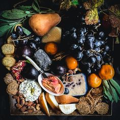 an assortment of fruits, nuts and cheeses on a wooden platter with leaves