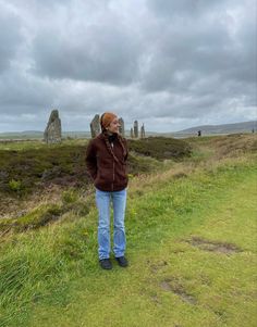 a woman standing on top of a lush green field next to stonehenge in the distance