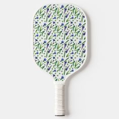 a ceramic paddle with blue flowers and green leaves on the front, against a white background