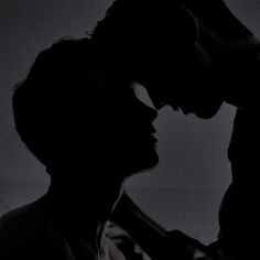 a man and woman are silhouetted against a dark background with their heads touching each other