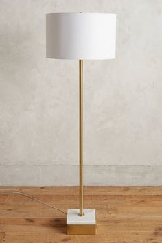 a floor lamp with a white shade on the base and a wooden floor in front of it