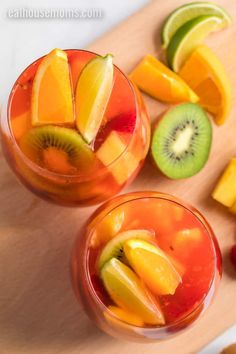 two glasses filled with fruit on top of a wooden cutting board