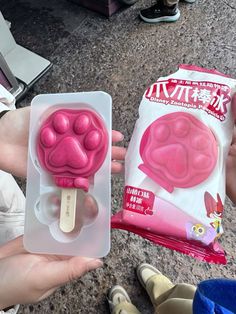 a person holding up a pink popsicle shaped like a dog's paw