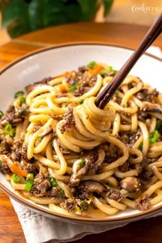 noodles with meat and vegetables in a white bowl on a wooden table next to chopsticks