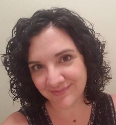 a close up of a person with curly hair smiling at the camera and wearing a tank top